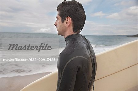 Jeune homme en combinaison holding sa planche de surf