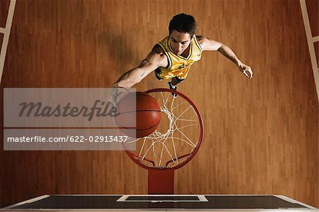 Young man jumping to slam dunk basketball in hoop