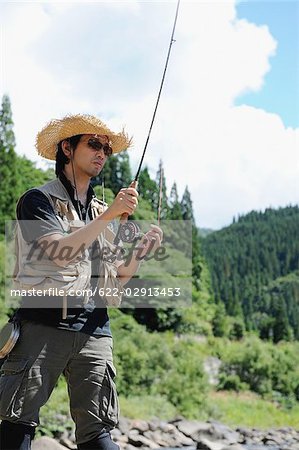 Homme avec chapeau de paille debout et tenant la canne à pêche