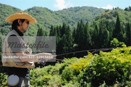 Homme avec chapeau de paille debout et tenant la canne à pêche