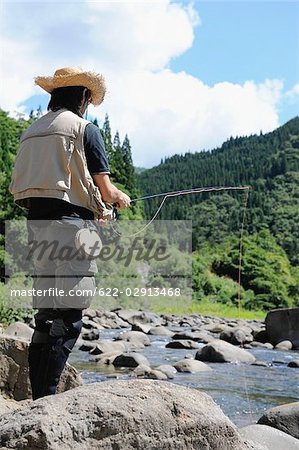 Homme avec chapeau de paille debout sur la pierre et la tenue de canne à pêche