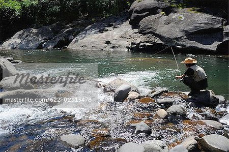 Homme avec chapeau de paille assis sur la pierre et la pêche