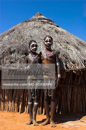 Hamer girls standing in front of house, wearing traditional goat skin dress decorated with cowie shells, Dombo village, Turmi, Lower Omo valley, Ethiopia, Africa