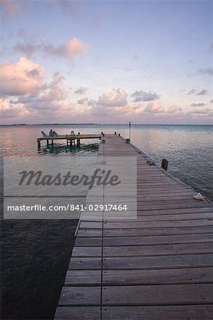 People sitting on chair on jetty at sunrise, Tobaco Caye, Belize, Central America