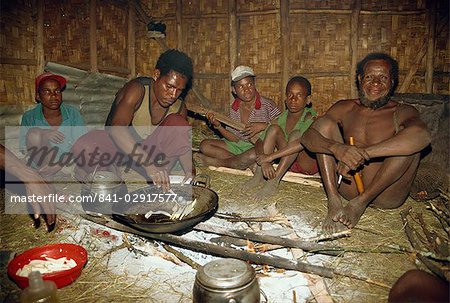 Dani men inside house, preparing dinner and playing wooden guitar, South Beliam Valley, Irian Jaya, Indonesia, Southeast Asia, Asia