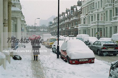 Femme avec parapluie et voitures recouvert de neige en hiver à West Kensington, Londres, Royaume-Uni, Europe