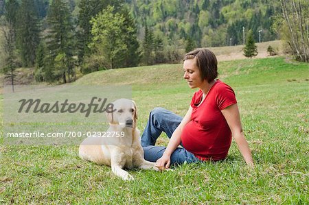 Pregnant Woman Sitting in Field With Her Dog