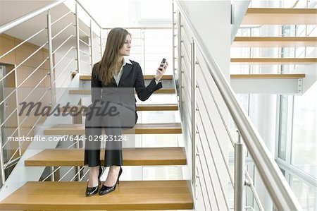 Businesswoman looking at cell phone on office staircase