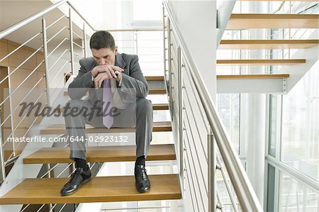 Businessman on office staircase with head on hands