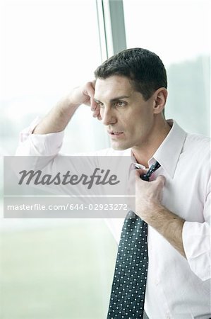 Homme d'affaires regardant par la fenêtre, régler la cravate