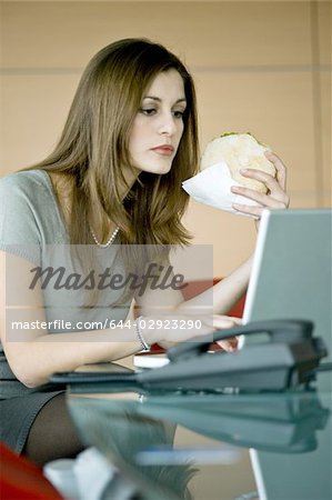 Femme d'affaires, manger un sandwich pita à ordinateur portable