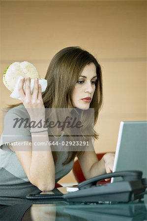 Femme d'affaires, manger un sandwich pita à ordinateur portable