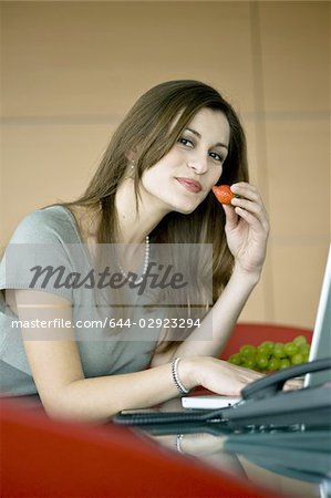 Businesswoman eating a strawberry at laptop