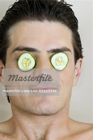 Jeune homme avec des tranches de concombre sur les yeux