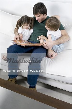 Junger Mann auf der Couch mit Kindern lesen