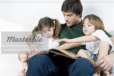 Junger Mann auf der Couch mit Kindern lesen