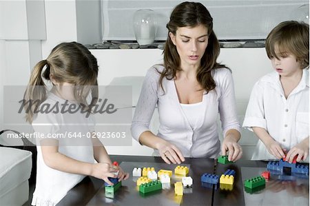 Young woman and boy and girl playing with building blocks