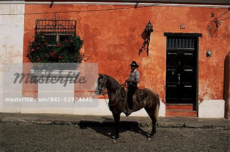 Mann auf dem Pferd vor einer typischen bemalten Wand, Antigua, Guatemala, Zentralamerika