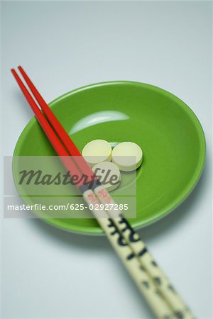 Close-up of three pills in a bowl with two chopsticks