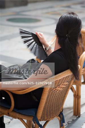 Side profile of a woman sitting on chair and holding a folding fan, Naples, Naples Province, Campania, Italy
