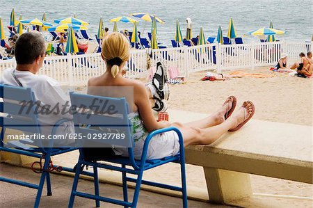 Vue arrière d'un couple assis dans un fauteuil sur la plage, Plage De La Croisette, Cannes, Provence-Alpes-Cote d'Azur, PACA, France