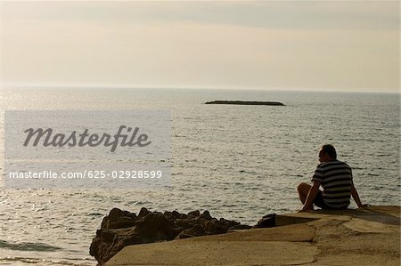 Vue arrière d'un homme assis sur l'oceanside, Biarritz, France