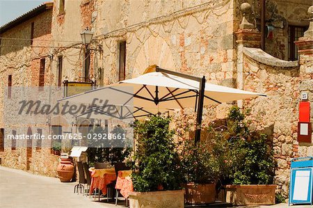 Getopfte Pflanzen und Sonnenschirme Terrasse vor einem Gebäude, Piazza Roma, Monteriggioni, Provinz Siena, Toskana, Italien