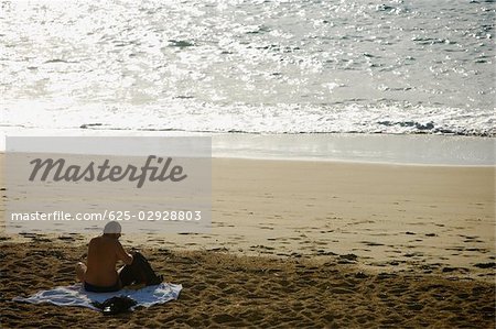 Vue arrière d'un homme assis sur la plage, Grande Plage, Biarritz, France