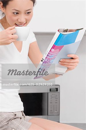 Side profile of a young woman drinking tea and reading a magazine