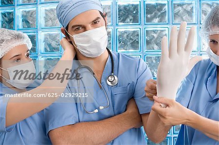 Two female surgeons adjusting surgical glove and surgical mask of a male doctor