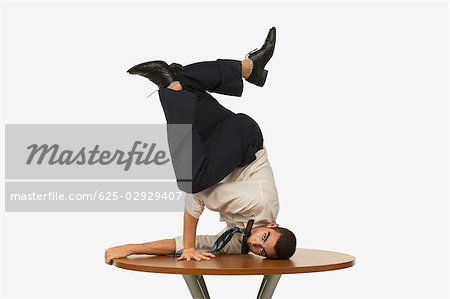 Portrait of a businessman doing a handstand on a table with a mobile phone in his mouth