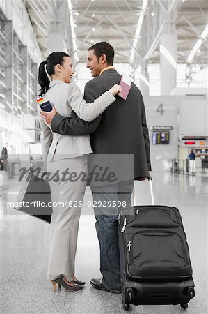 Businessman and a businesswoman standing at an airport with their arms around each other