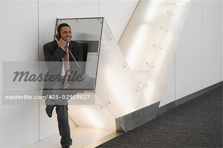 Businessman talking on a pay phone at an airport and smiling