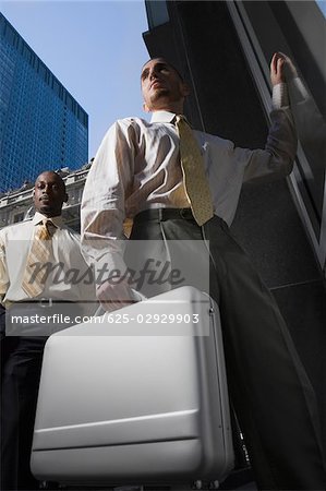 Low angle view of a businessman holding a briefcase and another businessman standing behind him