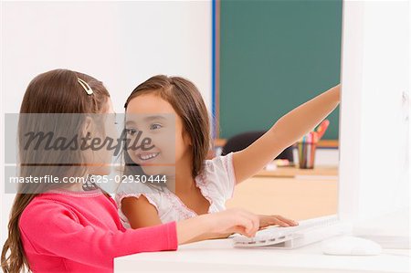 Profil de côté de deux écolières souriant devant un ordinateur
