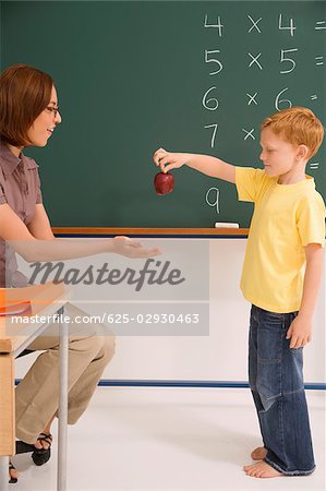Side profile of a schoolboy giving an apple to his female teacher in a classroom