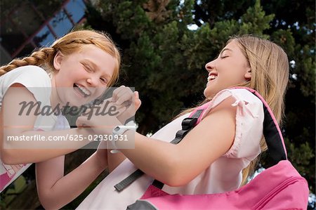 Low angle view of two schoolgirls playing clapping game and smiling