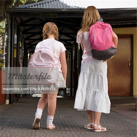 Rear view of two schoolgirls carrying schoolbags and walking