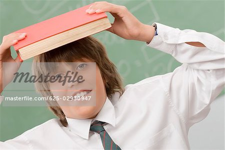 Portrait of a schoolboy holding a book over his head and smiling