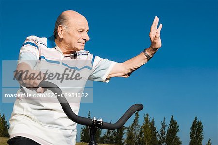 Senior homme sur une bicyclette et en agitant sa main