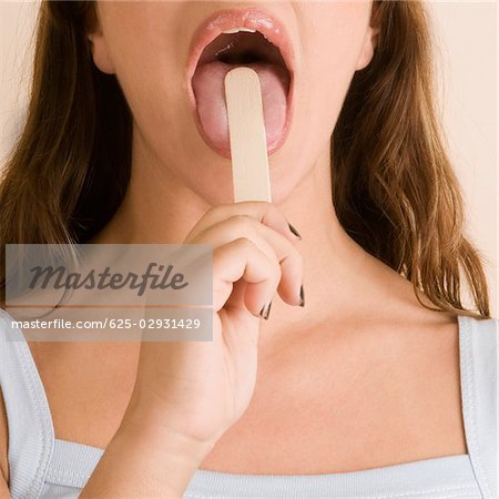 Nahaufnahme einer jungen Frau, die mit einer Zunge Depressor, ihre Zunge zu prüfen