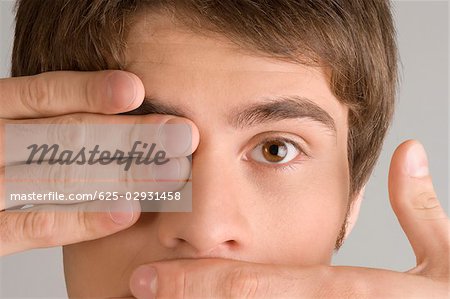 Close-up of a young man covering his mouth and his eye with his hands