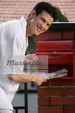 Portrait d'un jeune homme vérifiant sa boîte aux lettres et souriant