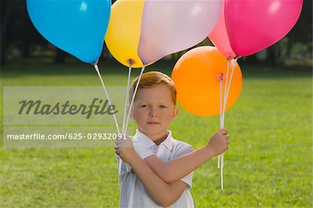 Portrait of a boy holding balloons in a park