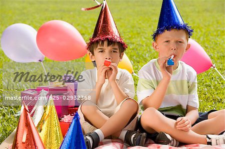 Two boys sitting together and blowing party horns
