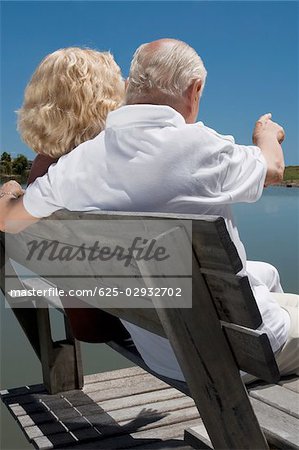 Rear view of a senior couple sitting on a bench at the lakeside