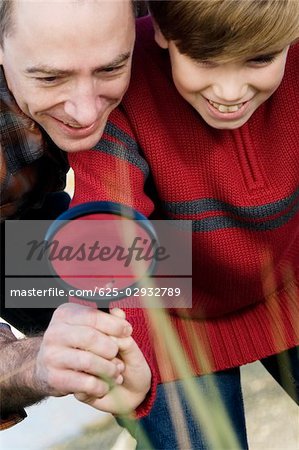 Low angle view of a mid adult man with his son holding a magnifying glass