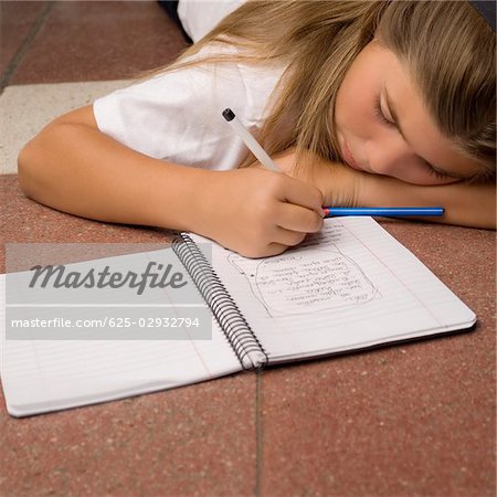 Schoolgirl lying on the floor and writing in a spiral notebook