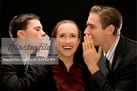 Side profile of two businessmen whispering to a businesswoman