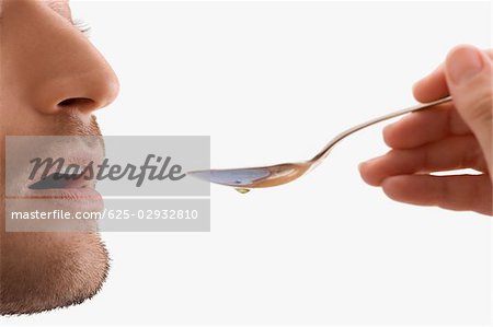 Mid adult man holding a spoon and taking medicine